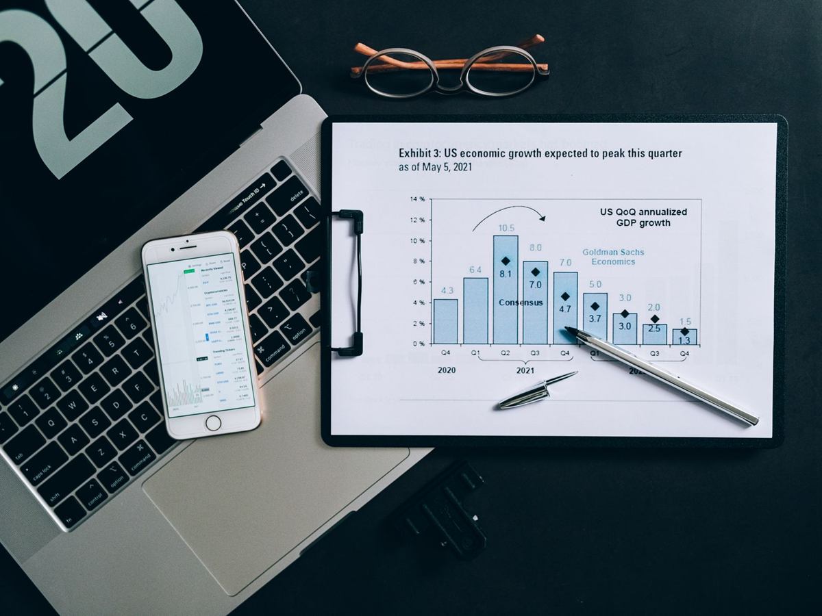 Laptop, Smartphone und Unterlagen mit Diagrammen auf einem Schreibtisch